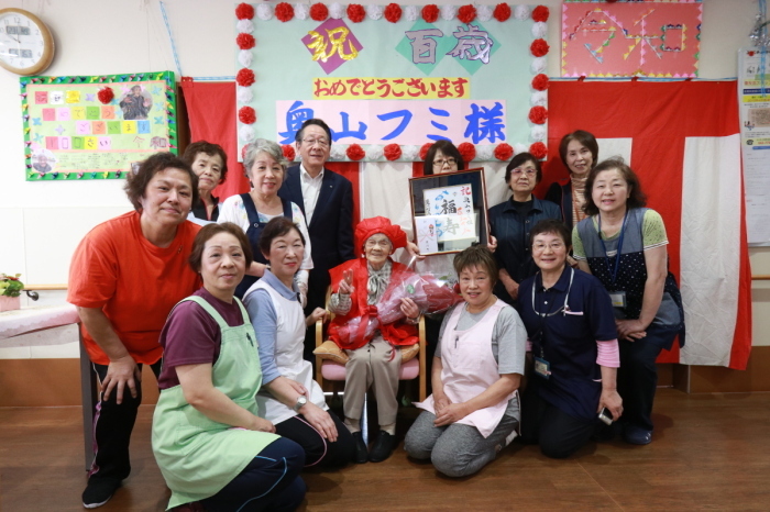 （写真）奥山さんとご家族、グループホームあいかわの皆さん、小野澤町長