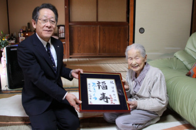 （写真）守屋さんにお祝いの額を渡す小野澤町長