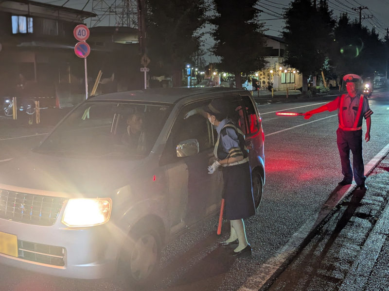 （写真）信号待ちの車のドライバーに啓発物品を手渡す交通指導隊員