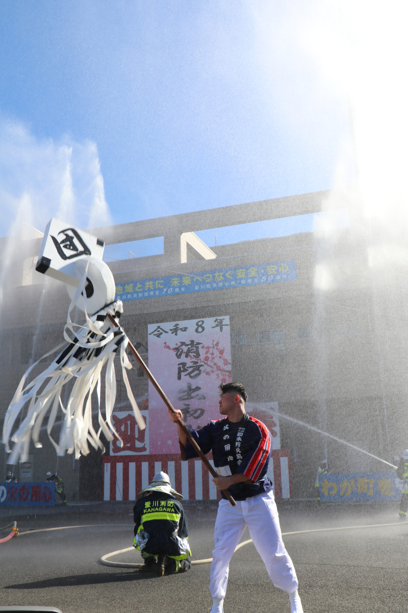 （写真）一斉放水演技と、纏を振る消防団員