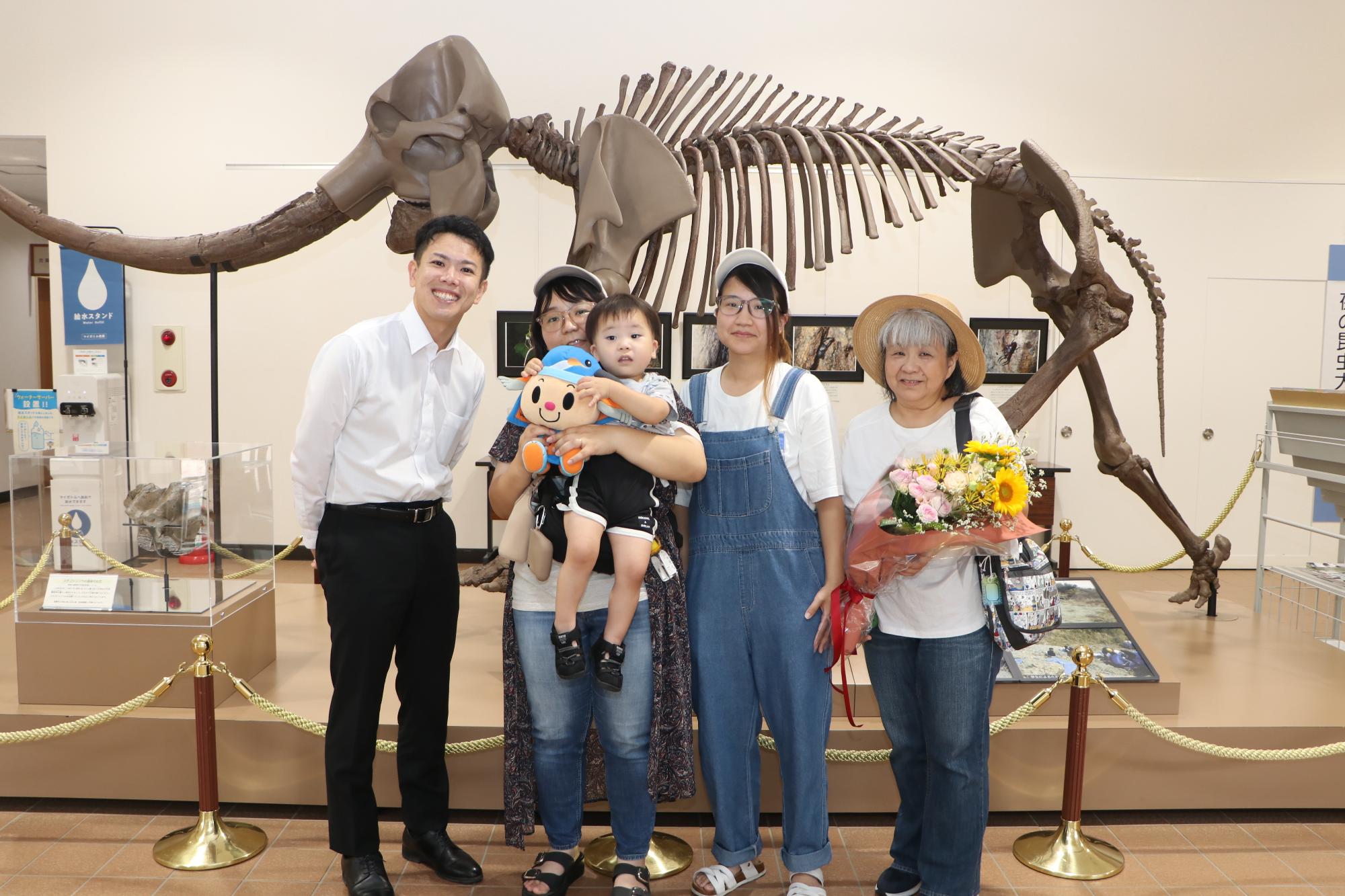 （写真）茅町長とあいちゃんぬいぐるみや花束を持って写る瑞穂さん、幸杜さん、ご親族の皆さん