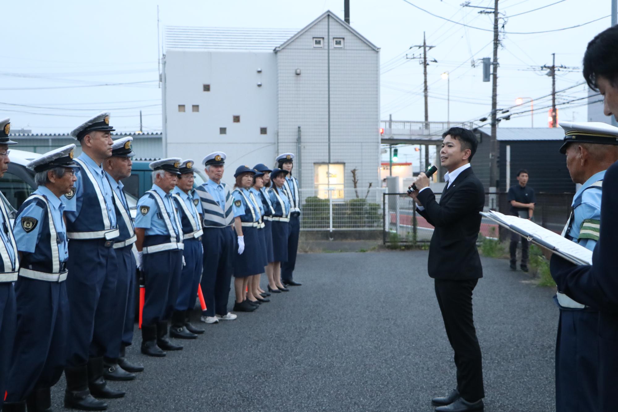 （写真）一列に並ぶ町交通指導隊の皆さんの前であいさつを述べる茅町長
