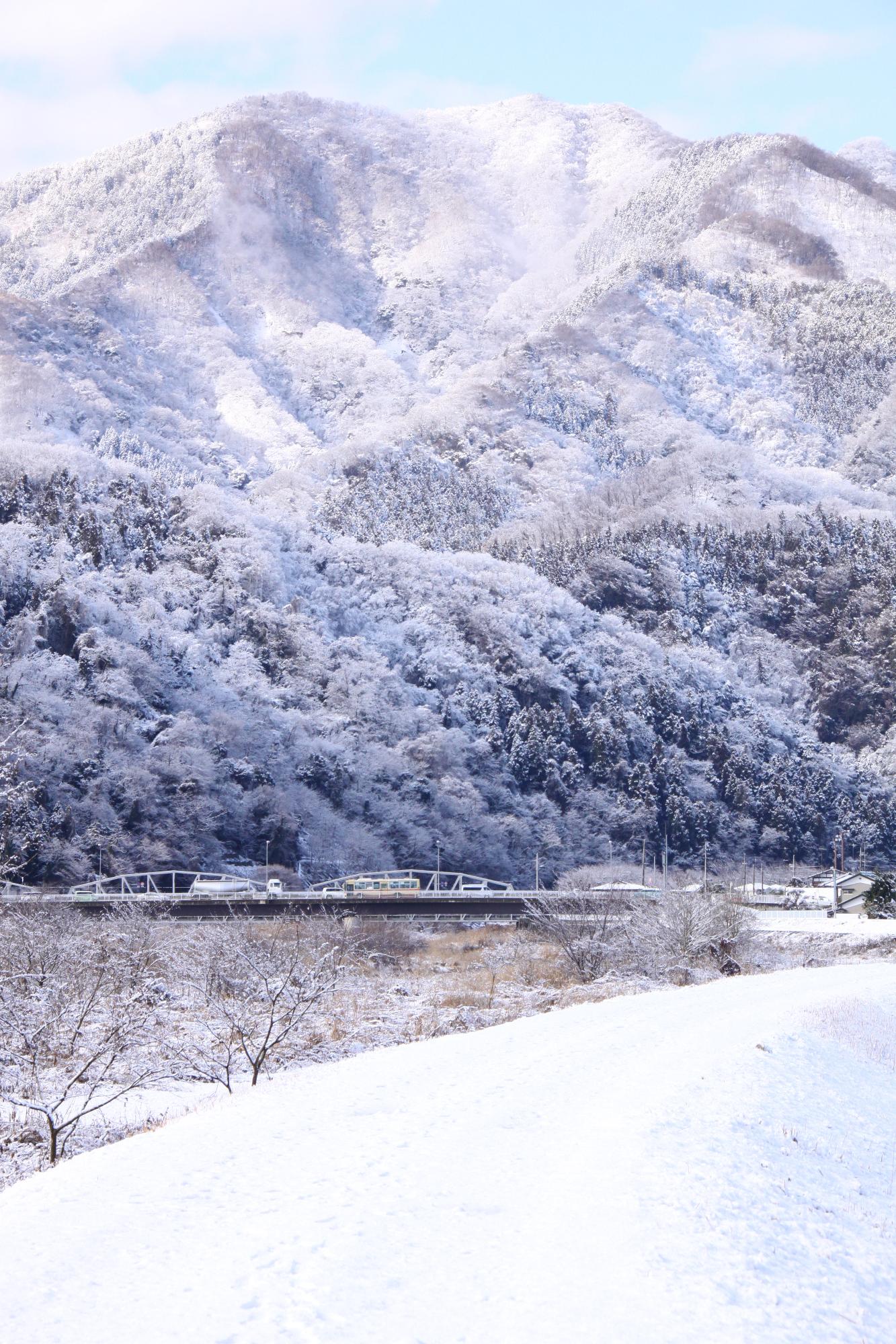 （写真）中津川の堤防と背景の山々の雪景色、中央には平山大橋と平山橋